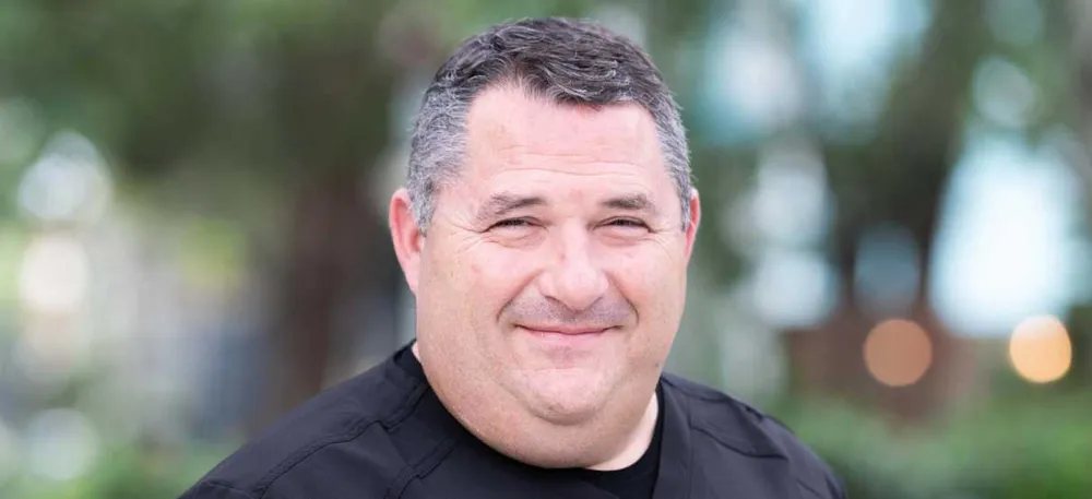 Dr. James A. Campo, a smiling dentist in black scrubs, photographed outdoors